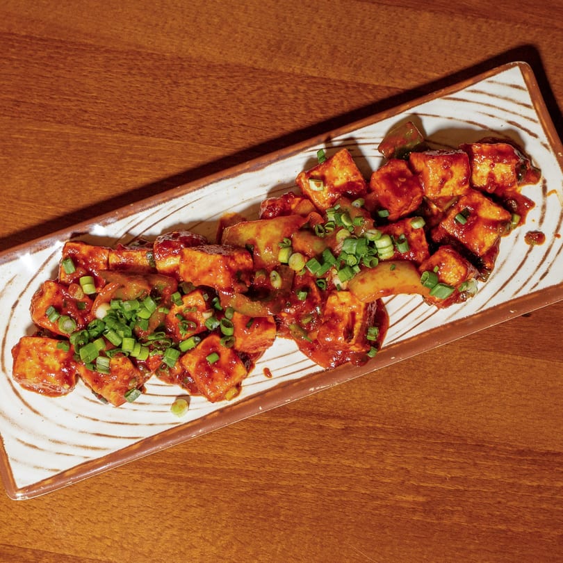 Manzil Fine Indian Dining's chili paneer, a vibrant dish of paneer cubes in red sauce, garnished with spring onions.