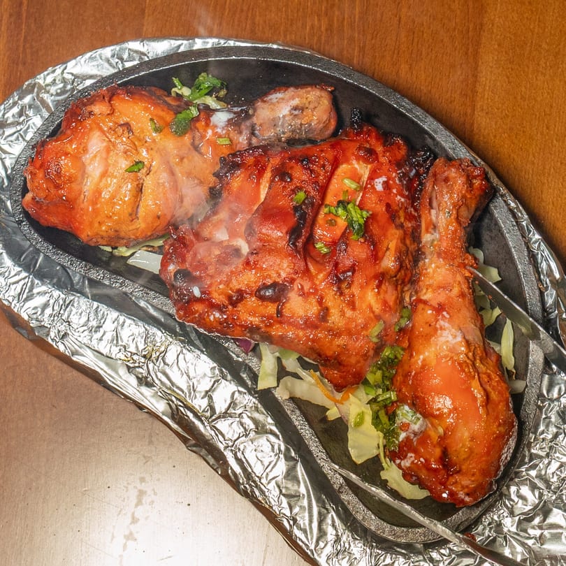 Steaming Indian Tandoori chicken, garnished with herbs, served on a hot platter with foil.