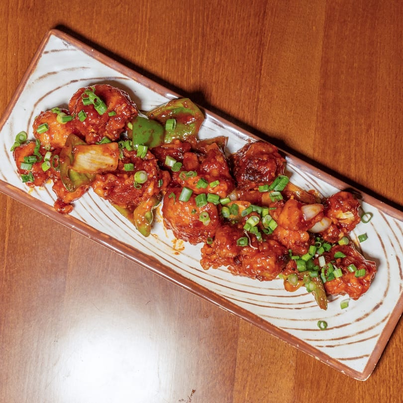 Manzil's chili chicken, a vibrant Indian dish with red sauce, green peppers, and scallions.