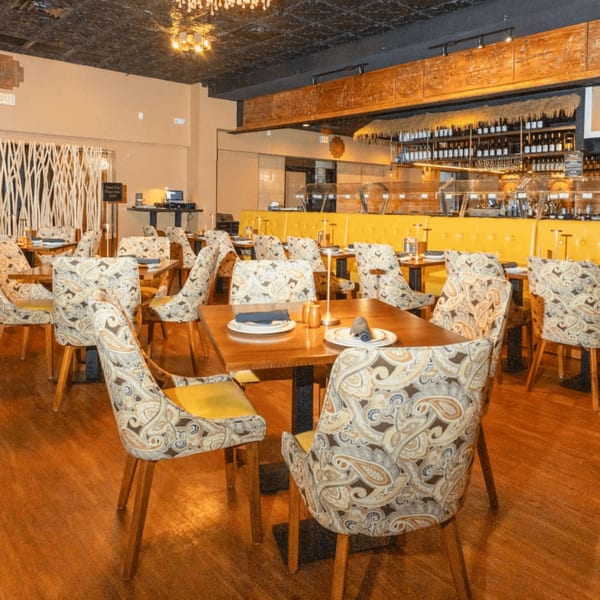 Manzil Fine Indian Dining interior with patterned chairs, wooden tables, and a yellow booth.