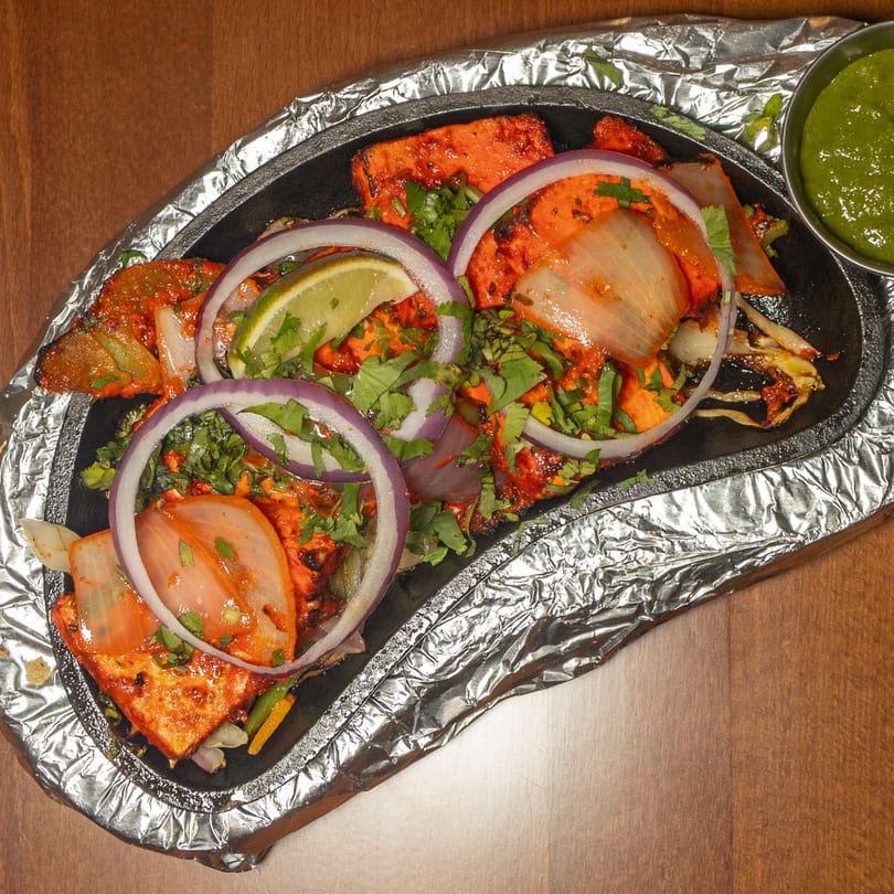 Manzil Fine Indian Dining's paneer tikka sizzler with onions, lime, cilantro, and green chutney.