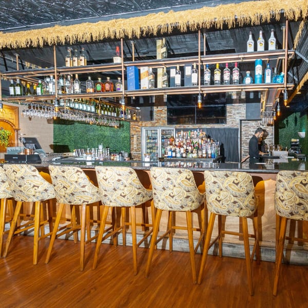 Manzil Fine Indian Dining bar with patterned stools, liquor bottles, and a bartender working.