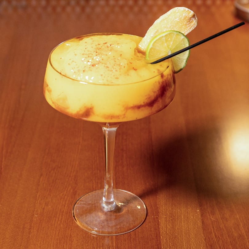 A Manzil Fine Indian Dining cocktail, yellow with a lime slice, candied ginger, and black straw.
