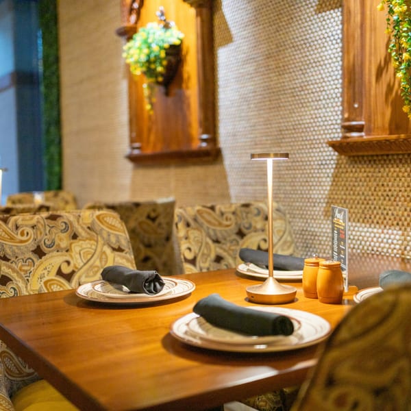 A set table at Manzil Fine Indian Dining with patterned chairs, plates, and a modern lamp.