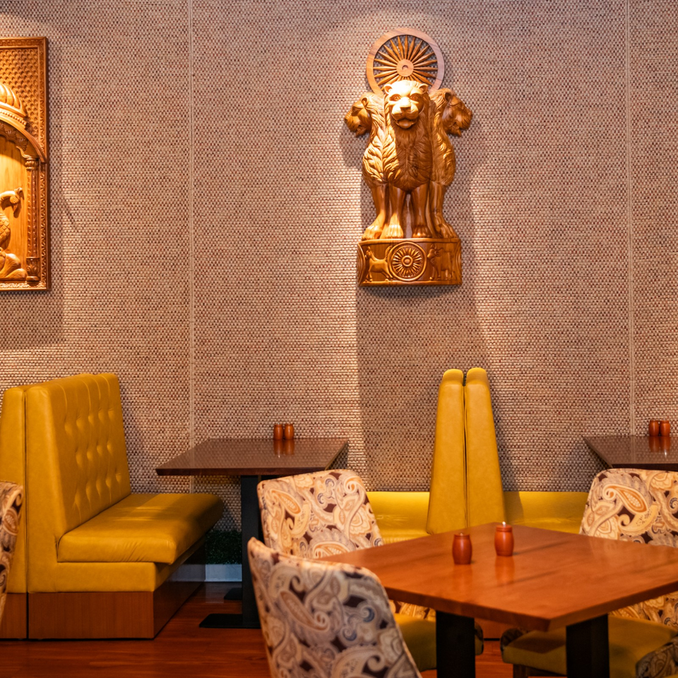 Elegant restaurant dining area with mustard-yellow booths, patterned chairs, wooden tables, and a gold lion sculpture mounted on the textured wall.