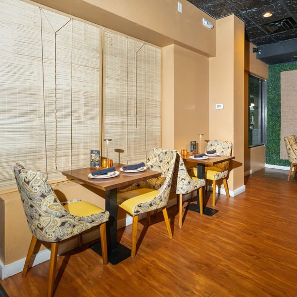 Manzil Fine Indian Dining interior with set tables, patterned chairs, bamboo blinds, and warm lighting.